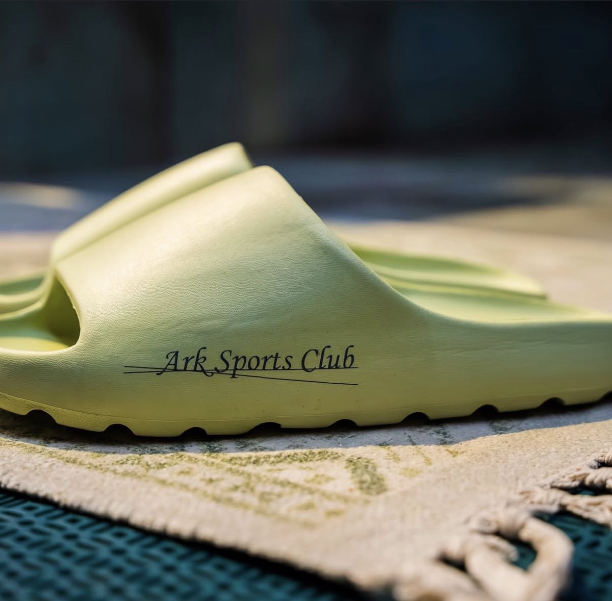 A pale green Ark Sports Club slide on a woven mat