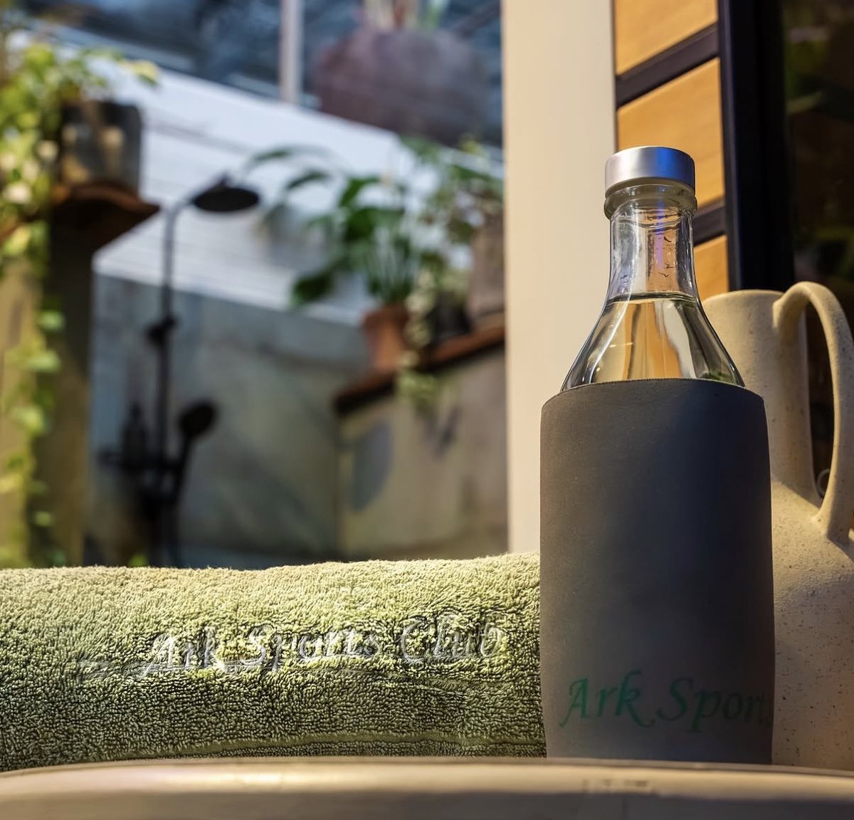A green Ark Sports Club towel beside an Ark water bottle, with the outdoor shower behind